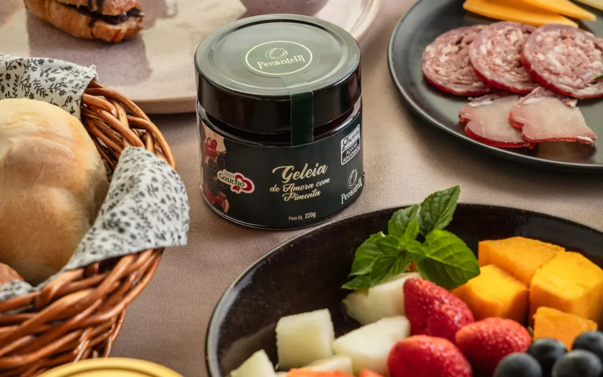 Mesa com café, croissant com cobertura de chocolate, frutas variadas, embutidos, queijo, pão, geleia em pote e xícara de café