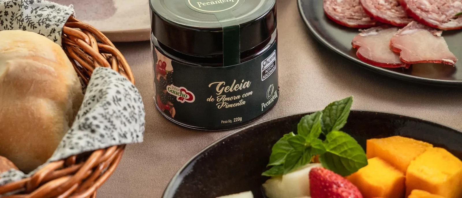 Mesa com café, croissant com cobertura de chocolate, frutas variadas, embutidos, queijo, pão, geleia em pote e xícara de café